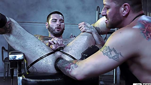 Tattooed big gay dude fists a Latino guy while wearing leather gloves